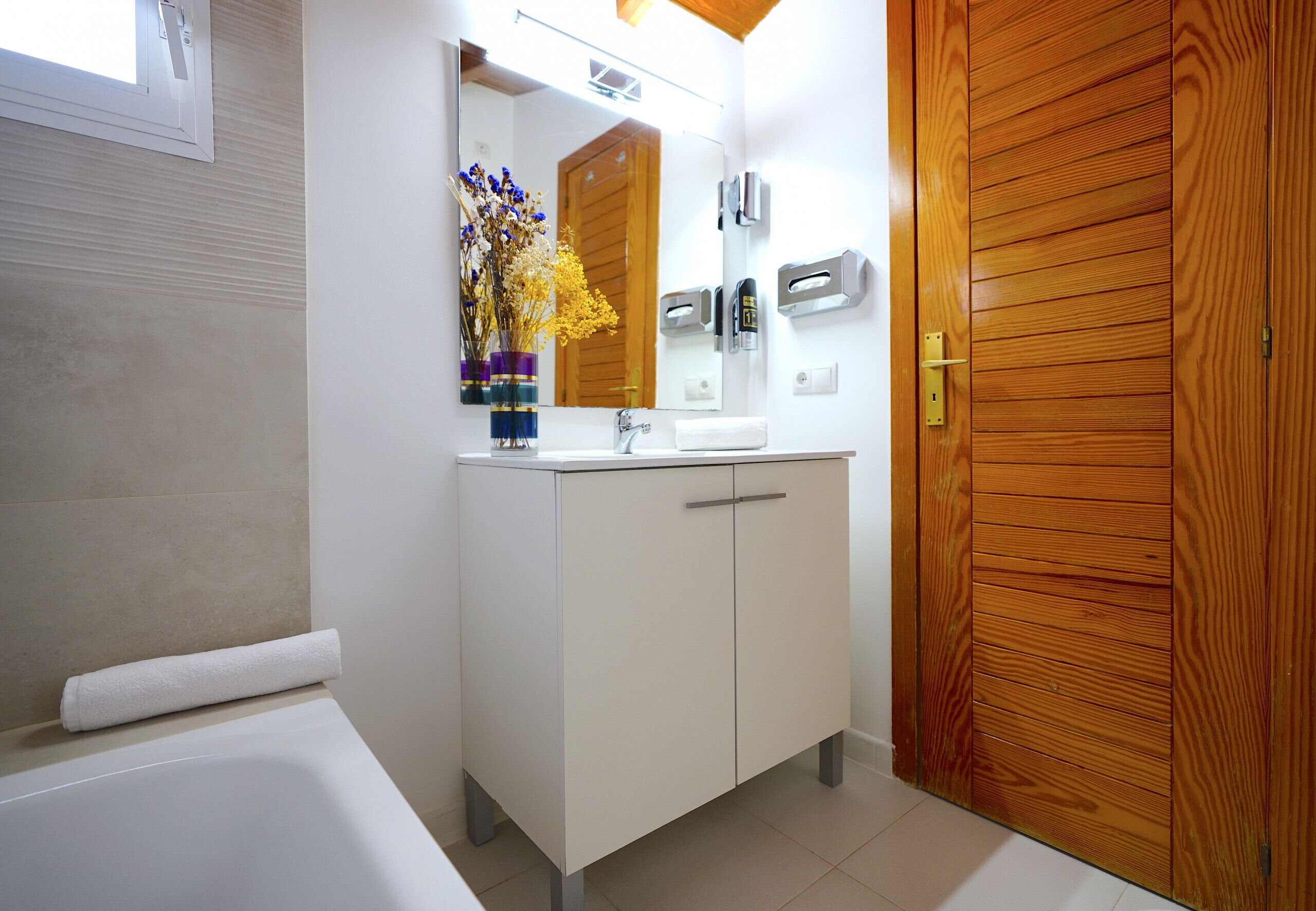 Une salle de bain avec un lavabo blanc, un miroir et une porte en bois.