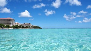 Un hotel frente a la playa con varias edificaciones, agua turquesa cristalina y cielo despejado.