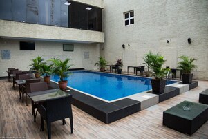 Zona de piscina interior con suelo de baldosas, rodeada de asientos y plantas en macetas.