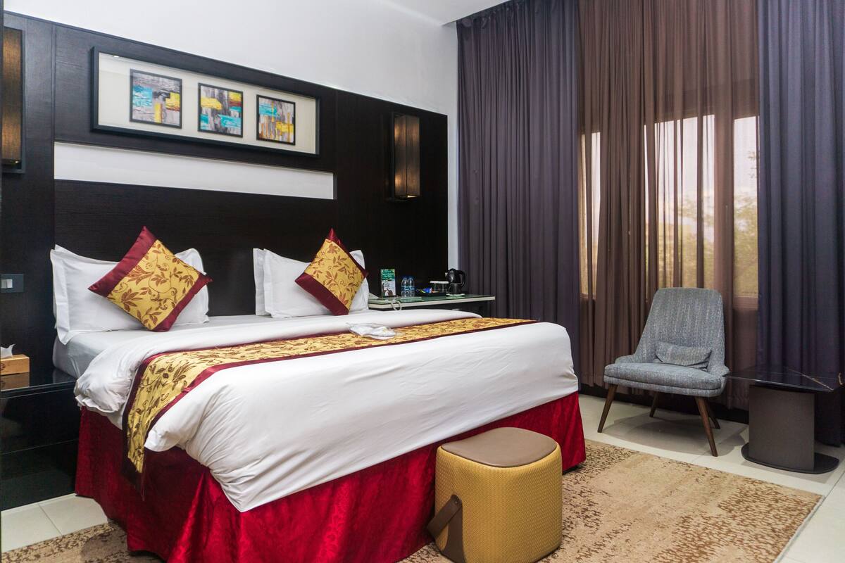 Habitación de hotel con una cama grande, una silla, una mesita y vistas al exterior.