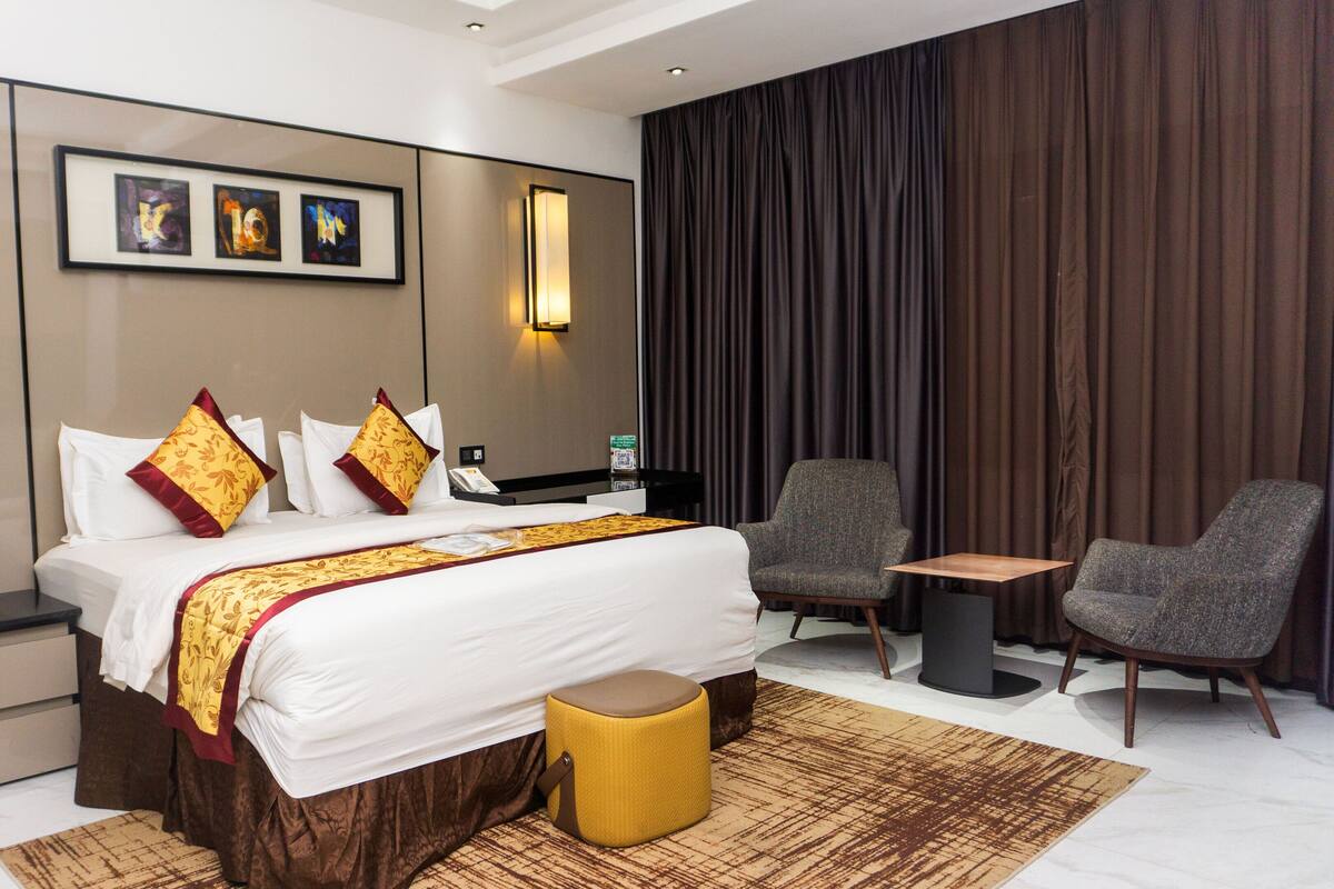 Una habitación de hotel moderna con una cama grande, dos sillones, una mesita y una mesita de noche con lámpara.