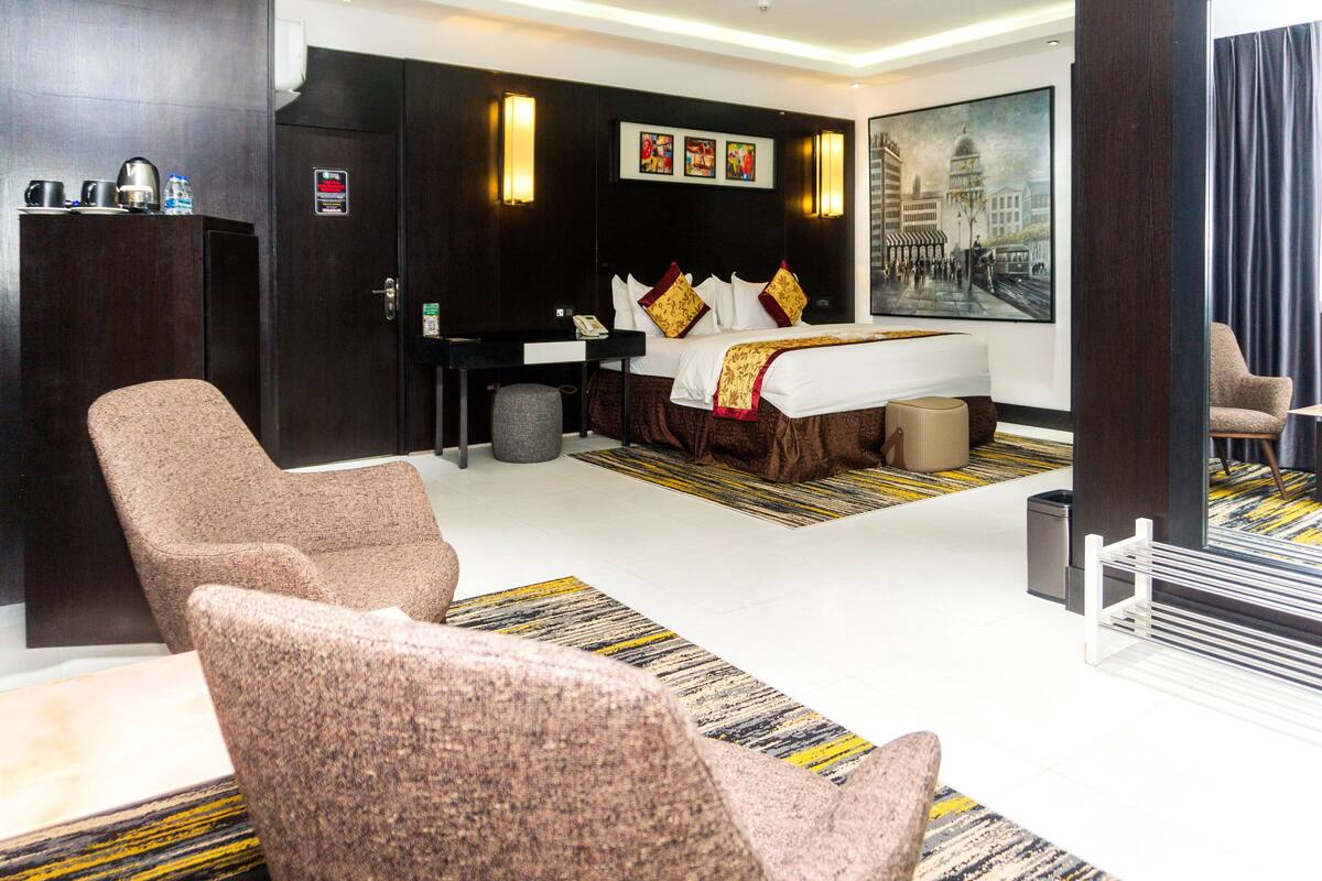 Habitación de hotel con cama, dos sillones, un escritorio y un cuadro en la pared.