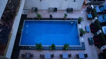 An aerial view of a rooftop swimming pool with surrounding lounge areas and a parking lot.