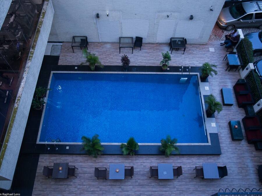 An aerial view of a rooftop swimming pool with surrounding lounge areas and a parking lot.