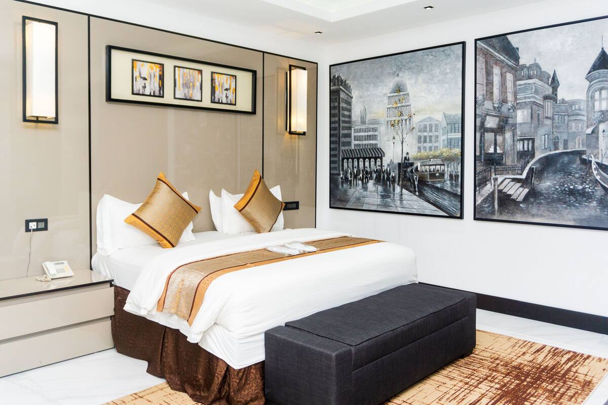 Una habitación de hotel moderna con una cama grande, una mesita de noche con un teléfono y un banco. Hay tres cuadros en la pared.