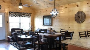 Un interior de madera con zona de comedor, cocina y un reloj en la pared.