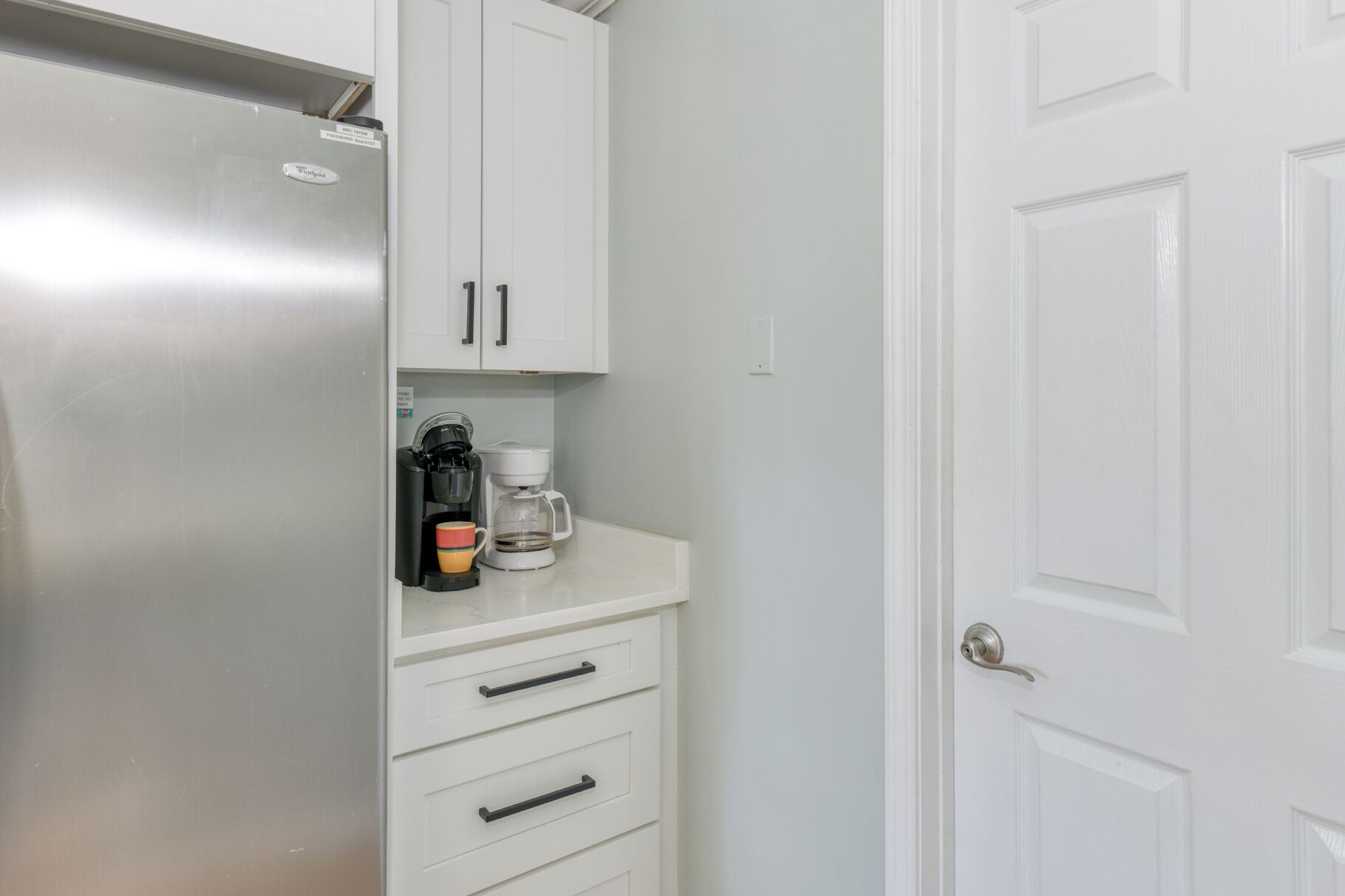 A compact kitchen with a stainless steel refrigerator, a coffee maker, and a white countertop.