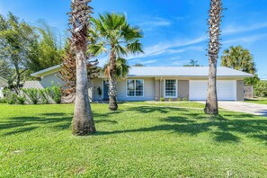 A single-story house with a garage, surrounded by well-maintained grass and palm trees.