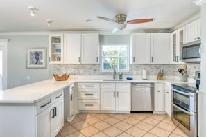 A modern kitchen with white cabinets, a dishwasher, an oven, and a ceiling fan.