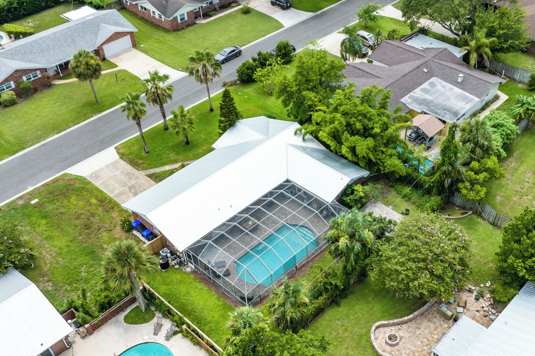 Vue aérienne d’un quartier résidentiel avec une grande maison dotée d’un vaste jardin comprenant une piscine et une serre.