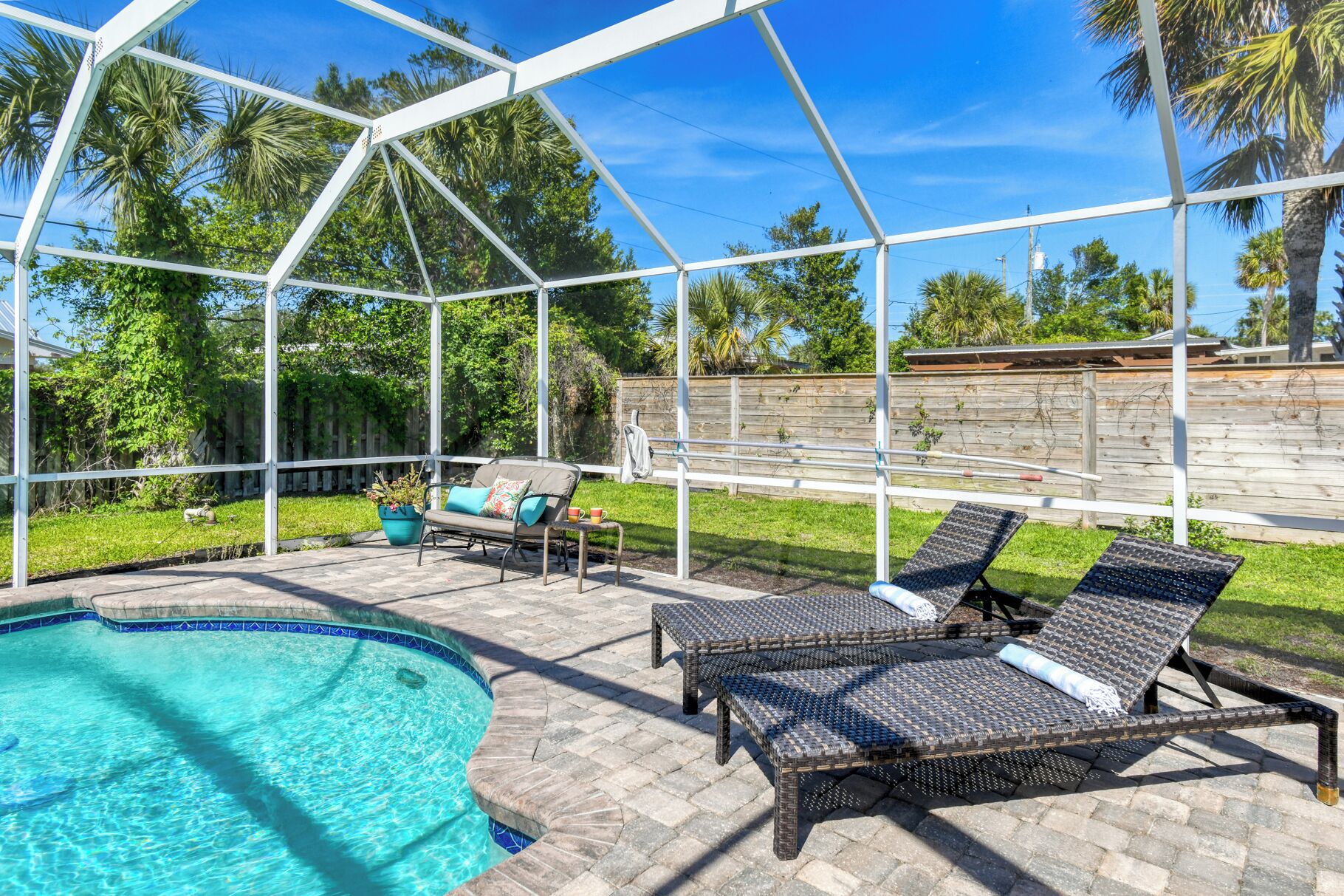 A covered outdoor area with a pool, lounge chairs, and a wooden fence.