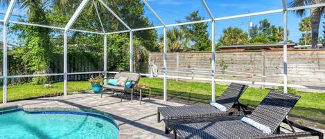 A covered outdoor area with a pool, lounge chairs, and a wooden fence.
