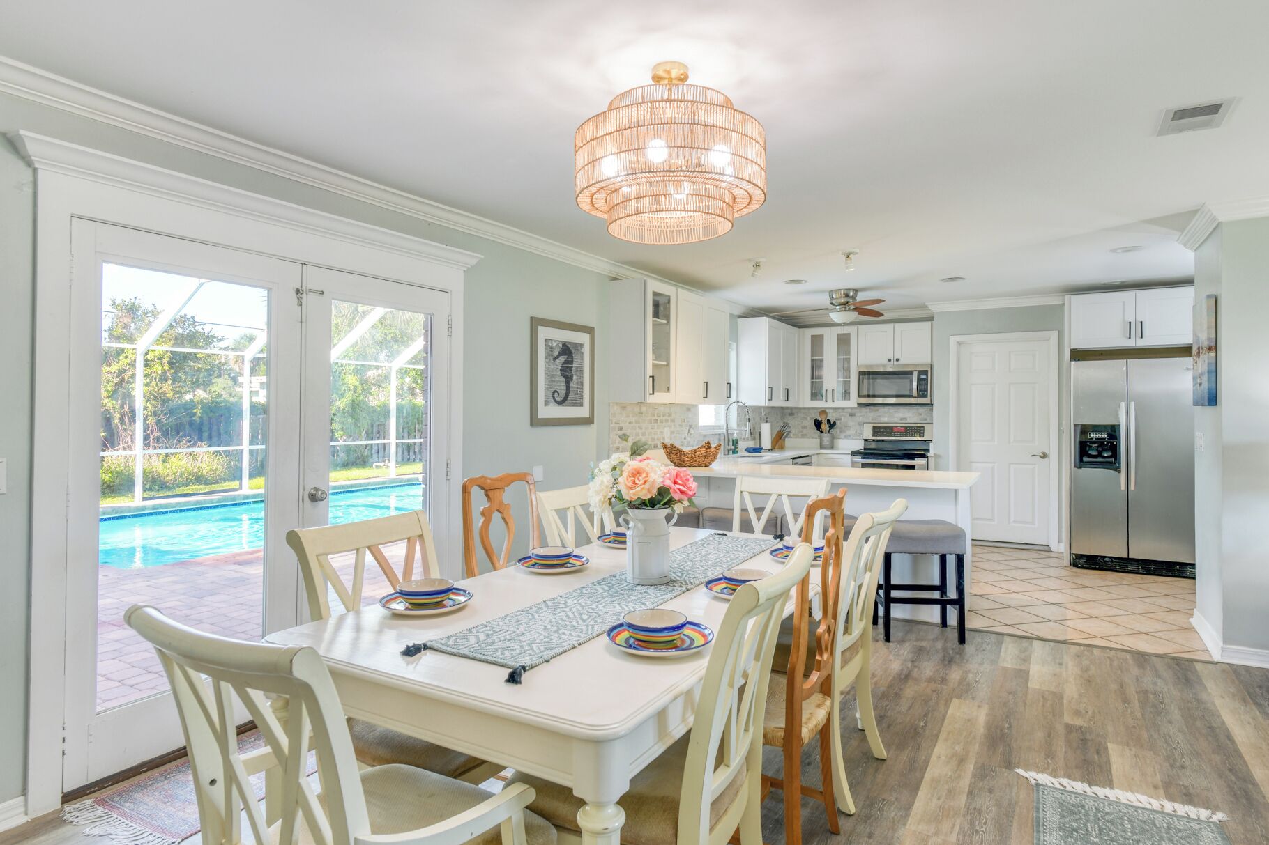 Uma área de refeições com vista para a piscina, uma cozinha com eletrodomésticos modernos e um candelabro.