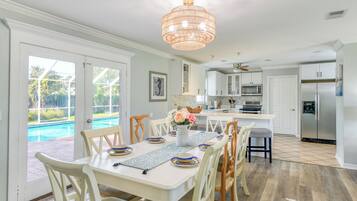 Uma área de refeições com vista para a piscina, uma cozinha com eletrodomésticos modernos e um candelabro.