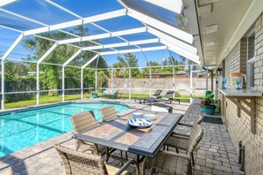 A covered outdoor pool area with a table and chairs, a glass enclosure, and a brick wall. - Southwind - Screened Heated Pool! Near Amphitheatre, Historic Downtown, & Beach (St. Augustine)