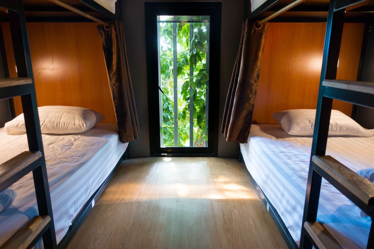 A room with two bunk beds, a window with a view of greenery, and a wooden floor.