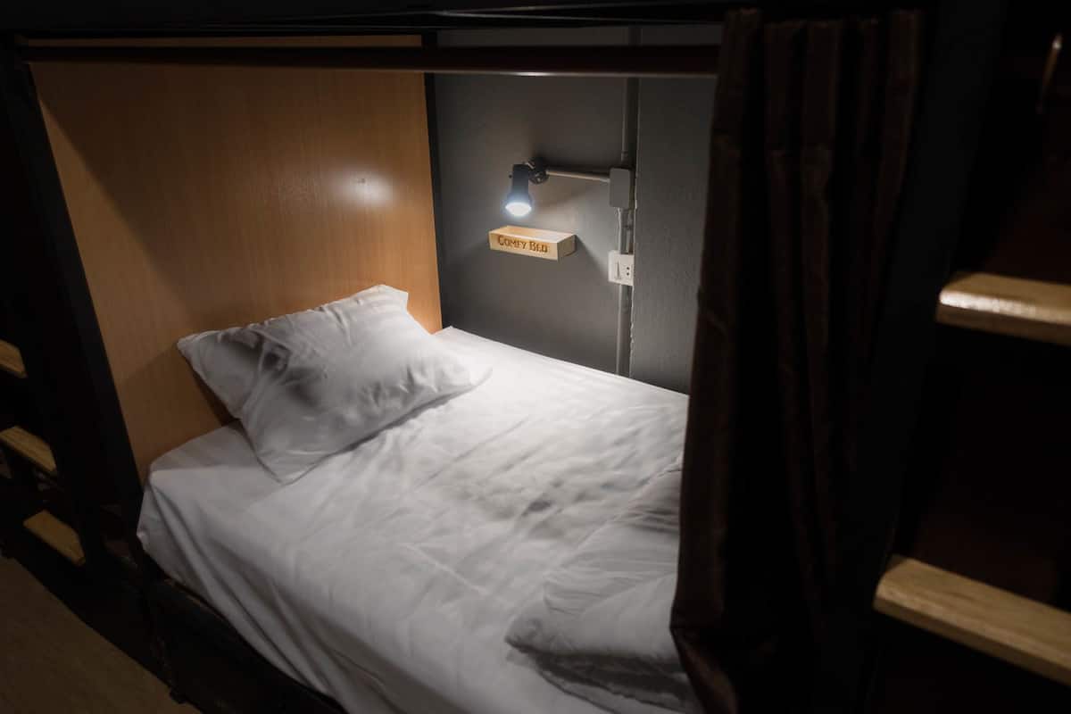 A single bed with a white mattress and pillow, a bedside table, a lamp, and a sign that reads "COMFY BED".