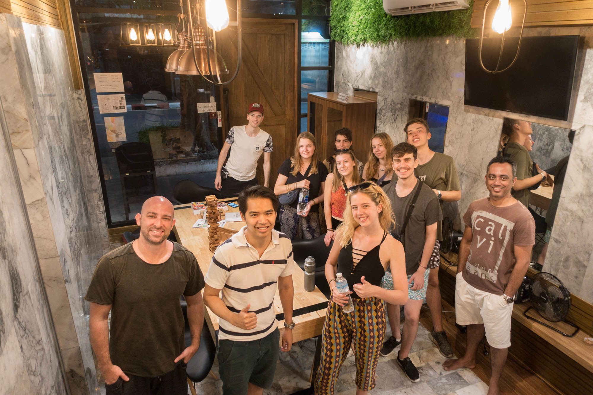 A group of people in a modern interior with marble walls, a wooden counter, and hanging pendant lights.