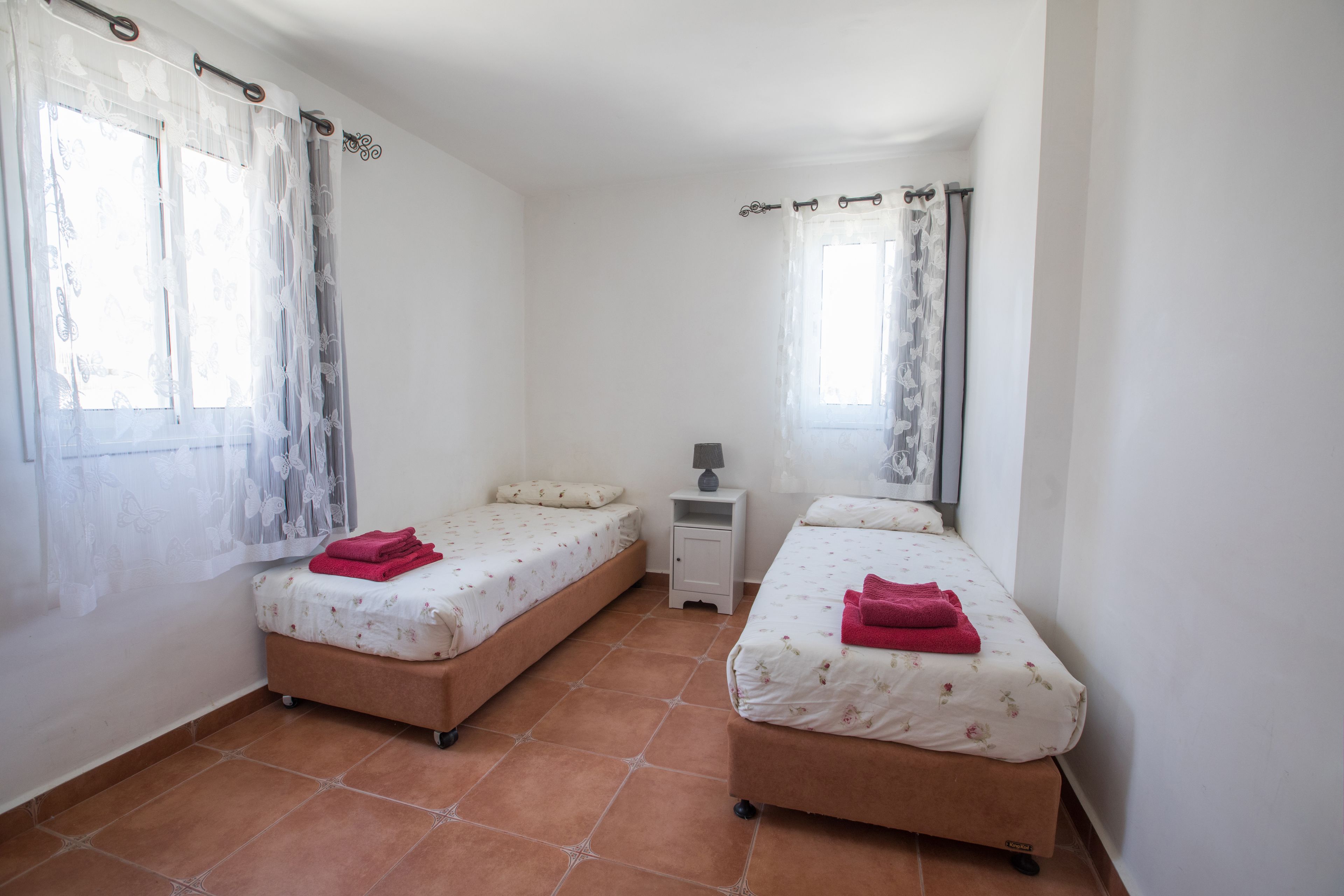 A small, clean room with two beds, a nightstand, and a window with curtains.
