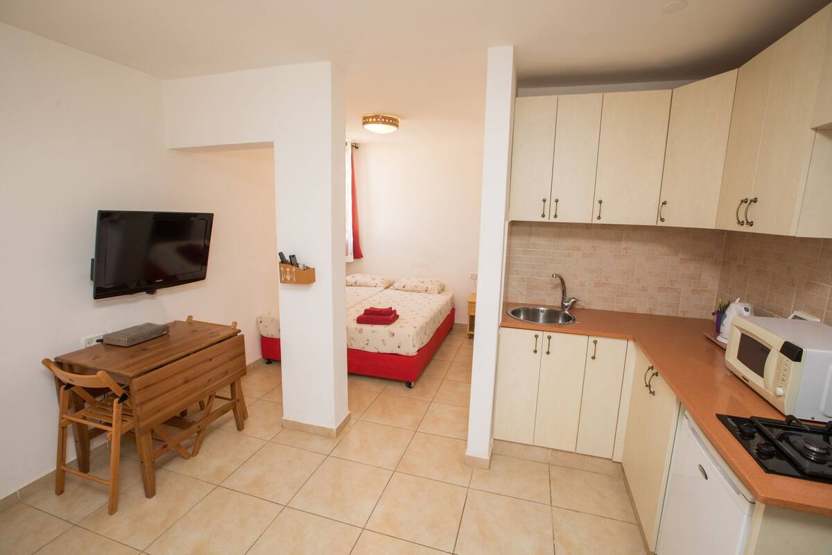A compact kitchen with a dining table, a bed, and a TV mounted on the wall.
