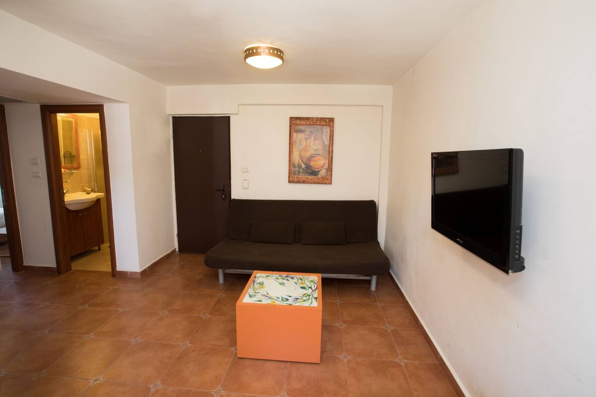 A living room with a sofa, a TV mounted on the wall, and a small orange table.
