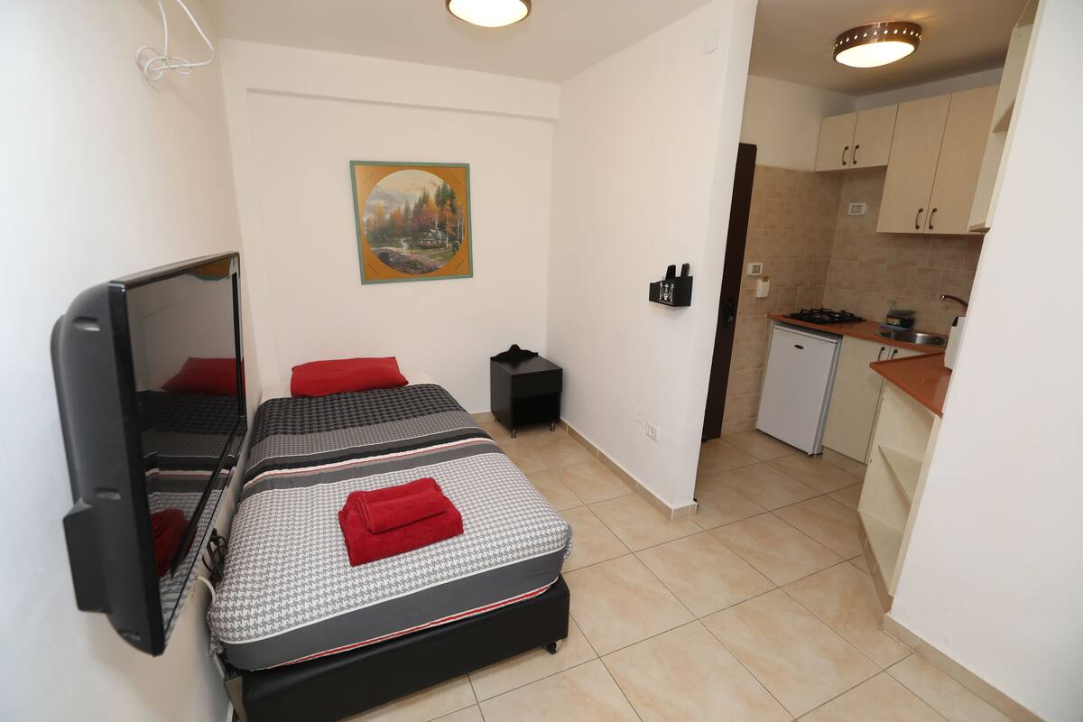 A compact room with two beds, a small kitchenette, and a painting on the wall.