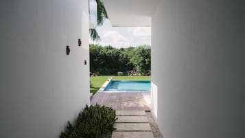 Stroll through the serene garden to the inviting pool area, surrounded by lush greenery and a wooden deck.