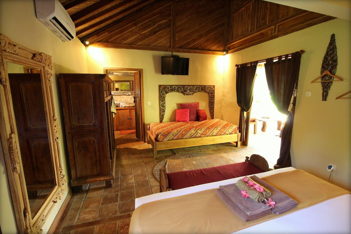 A bedroom with a wooden bed, a mirror, a television, and a bathroom visible through an open door.