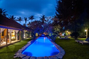 Una piscina con borde de piedra, rodeada por un césped cuidado y palmeras.