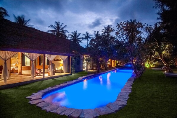 A poolside view of a resort with a clear pool, a thatched-roof building, and palm trees. - Dolcemare Resort (Gili Air)