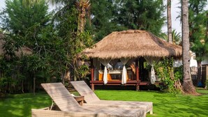A thatched-roof structure with a covered seating area, surrounded by lush greenery and a grassy lawn with two lounge chairs. - Dolcemare Resort (Gili Air)