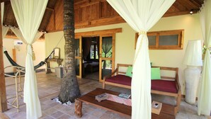 A cozy room with a wooden ceiling, a hammock, a sofa with cushions, and a table with a book. - Dolcemare Resort (Gili Air)