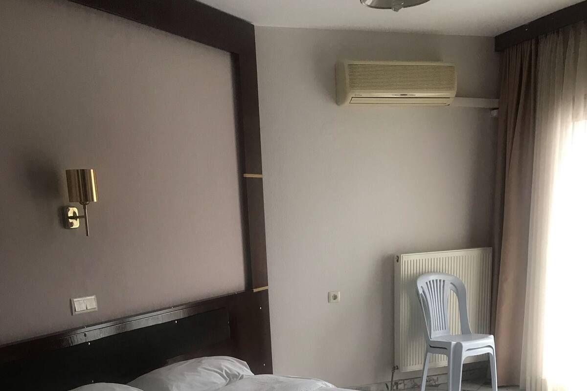 A hotel room with a large bed, a chair, an air conditioning unit, and a radiator.
