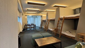 A modern dormitory room with bunk beds, a small seating area with a table, and a kitchenette in the background. - Tsuboniwa apartment UTSUBO (Osaka)