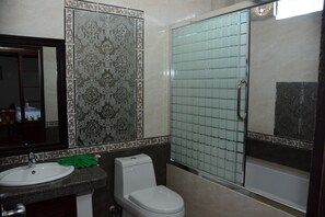 Bathroom features a classic design with a toilet, sink, and mirror, complemented by patterned tiles and a glass shower enclosure.
