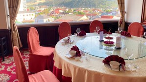 A dining area with a round table set for six, overlooking a scenic view of a town and hills. - Anoulackkhenlao Hotel (Phonsavan)