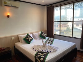 A hotel room with a bed, a bedside telephone, a wall-mounted air conditioner, and a window with curtains.