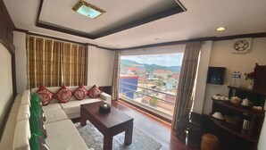 A living room with a sofa, a coffee table, and a view of a cityscape through large windows. - Anoulackkhenlao Hotel (Phonsavan)