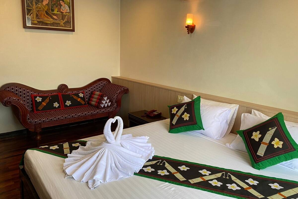 A hotel room with a bed, a wooden sofa, and a wall-mounted air conditioner.