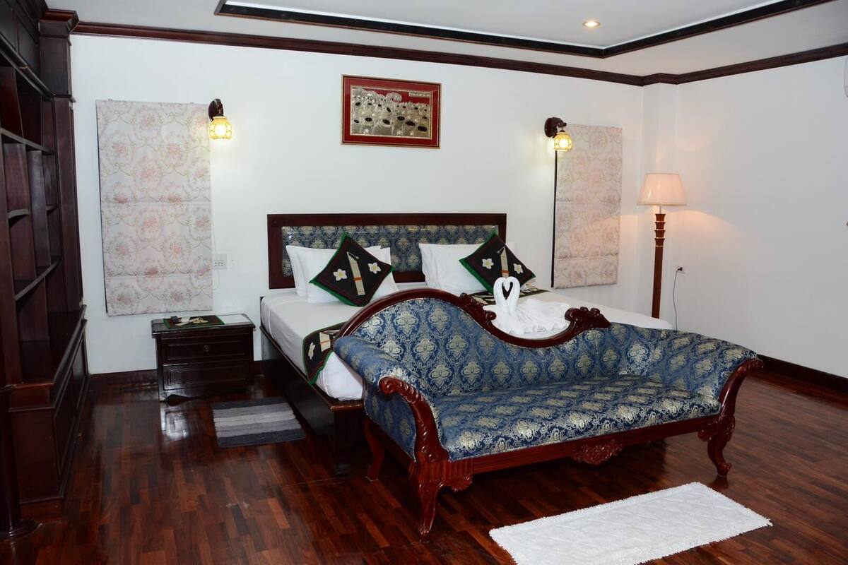 A bedroom with a wooden bed, a nightstand, a bedside table, a lamp, and a wall-mounted picture.