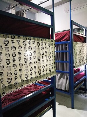 Camas literas con cortinas estampadas, un equipo de aire acondicionado a la vista y suelo de baldosas.