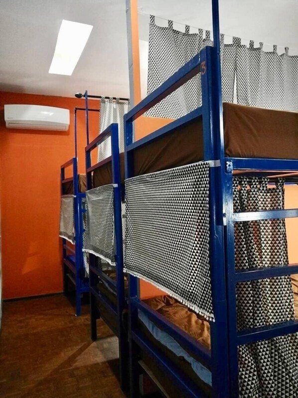Habitación con literas de estructura azul, aire acondicionado blanco y cortina con estampado en blanco y negro.