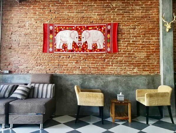 Una habitación con pared de ladrillo, un tapiz de elefantes, un sofá y dos sillones.