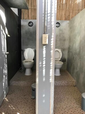 Un baño moderno con dos inodoros, un separador de metal y un techo de bambú.
