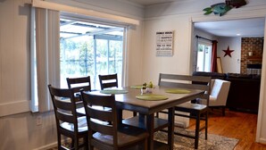 A dining area with a table and chairs, a kitchen in the background, and a wall with a family rules sign. - The Grey Goose (Waterfront) Historic New Bern - Private Beach - BRING YOUR BOAT! (New Bern)