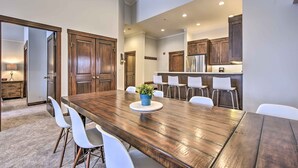 Una cocina moderna con armarios de madera, una amplia mesa de comedor con sillas blancas y una pequeña isla con taburetes de bar.