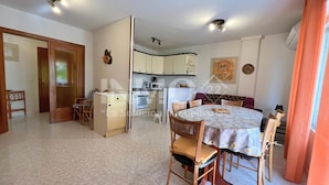 En kompakt opholdsstue med spiseplads, tekøkken og dør til et andet rum.