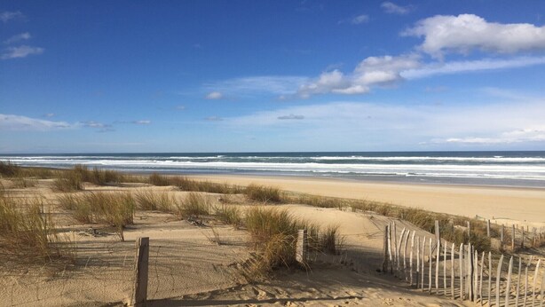 Una platja amb un camí de sorra, una tanca de fusta i l'oceà de fons.
