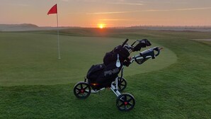 Camp de golf al capvespre, amb una bossa i un carro de golf al primer pla.