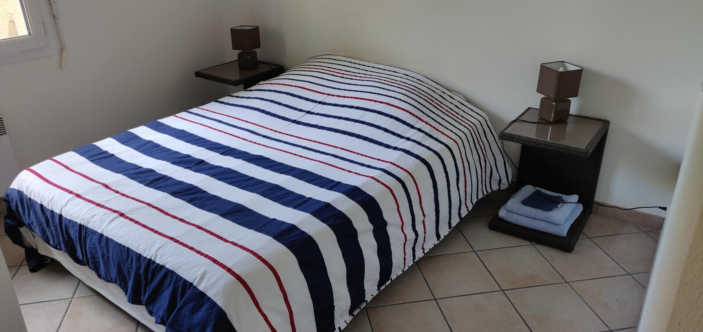 A neatly made bed with a striped bedspread, two bedside tables with lamps, and a folded towel on the floor.
